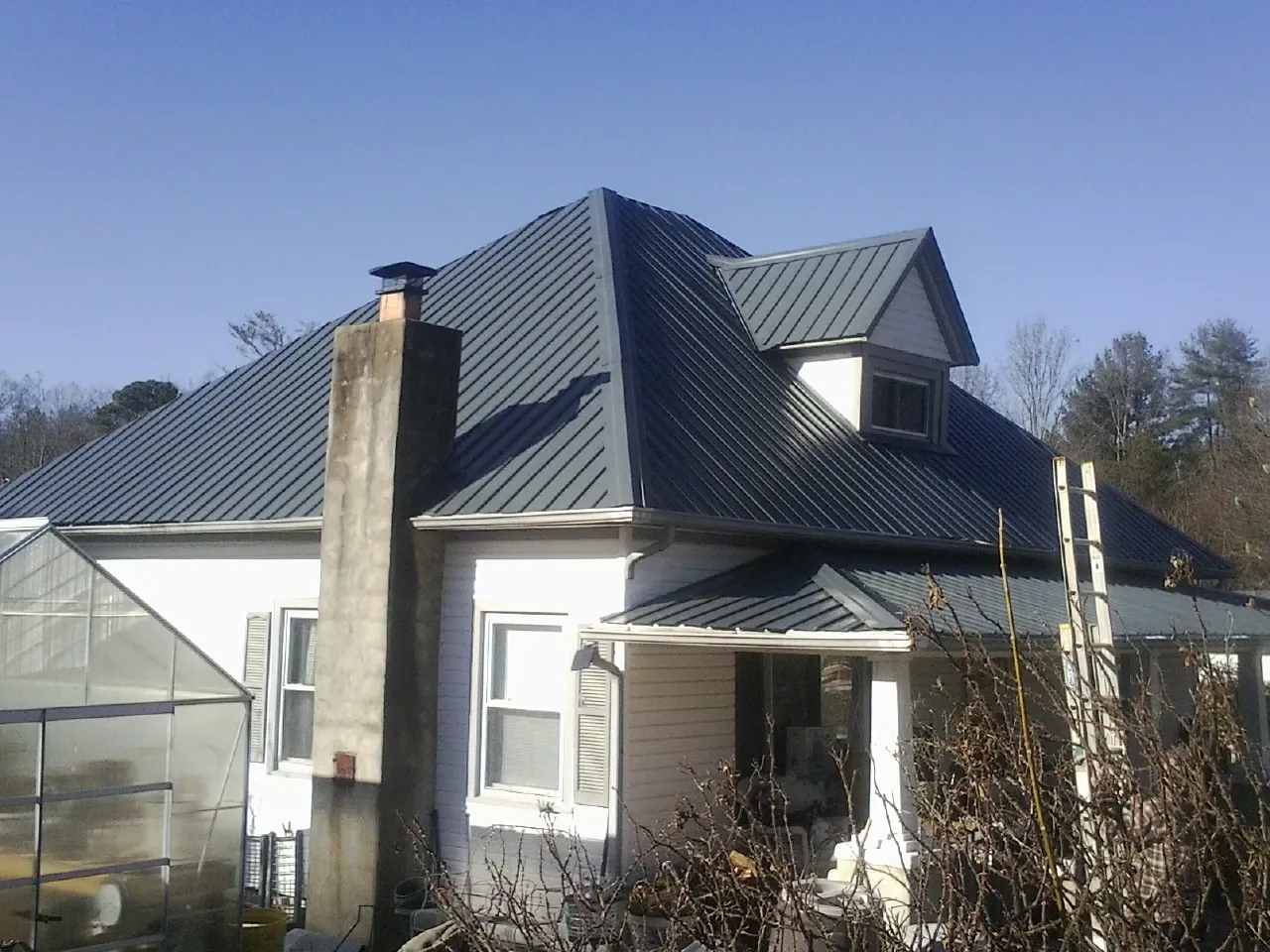 Dark blue standing seam metal roof on a white farmhouse with dormer — Slate & Tile Roof Repair by Roofing Brothers in Hartington