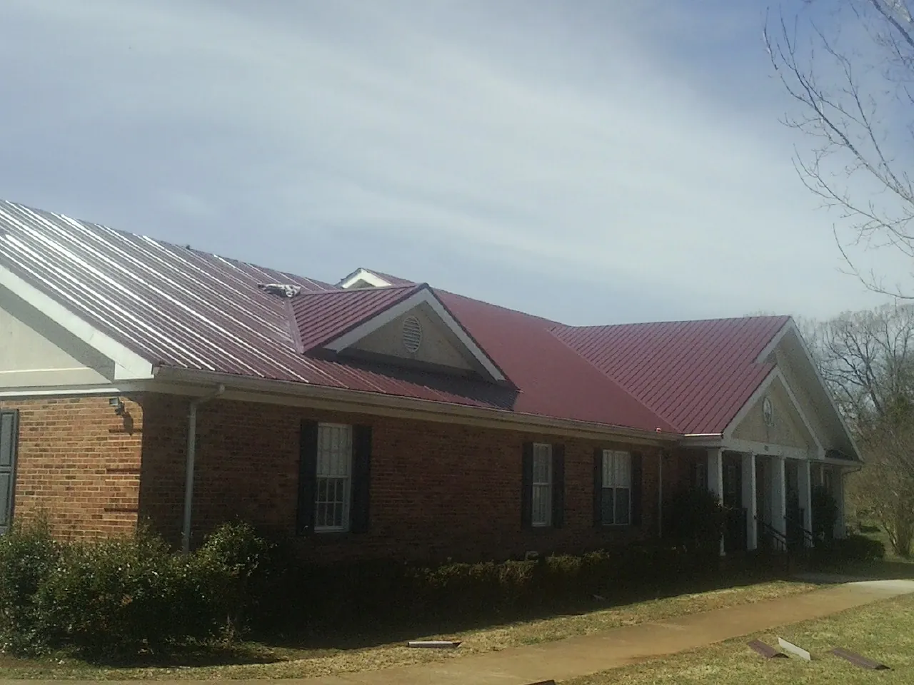 Red metal roof with gabled entries on a long brick building, from a Hail Damage Roof Repair job in Hartington
