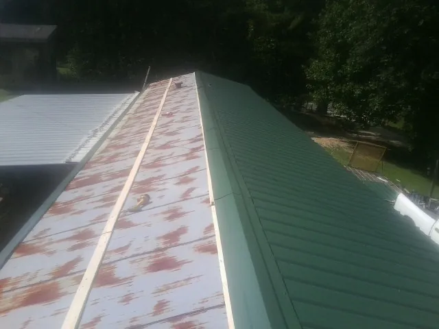 Old rusted panels beside newly installed green metal roofing — Wind Damage Roof Repair by Roofing Brothers in Hartington