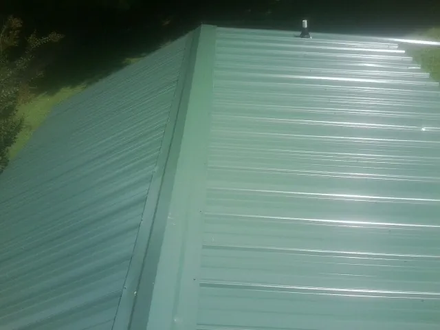 New green metal panels meeting at the ridge of a roof — Flat Roof Repair work by our crew in Hartington