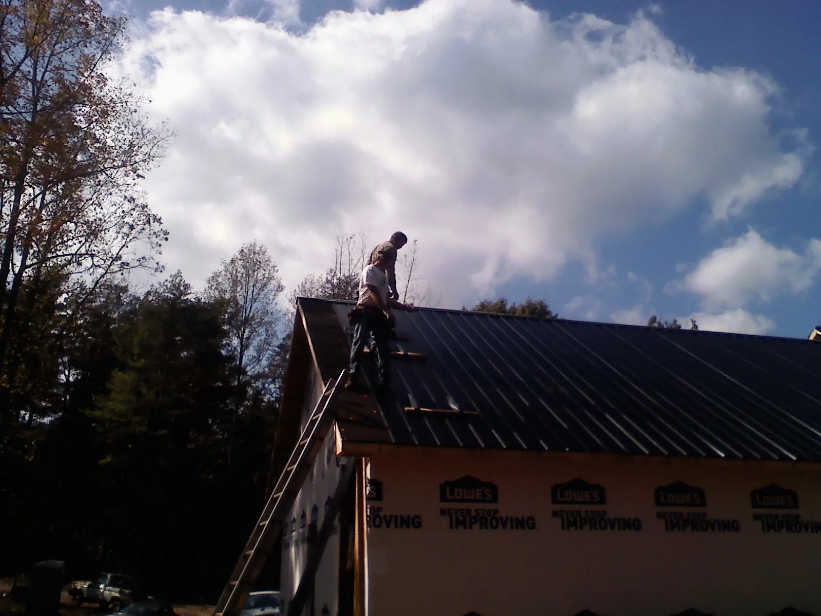 Roofer fastening dark metal panels high against a cloudy sky, from a Roof Inspection job in Hartington