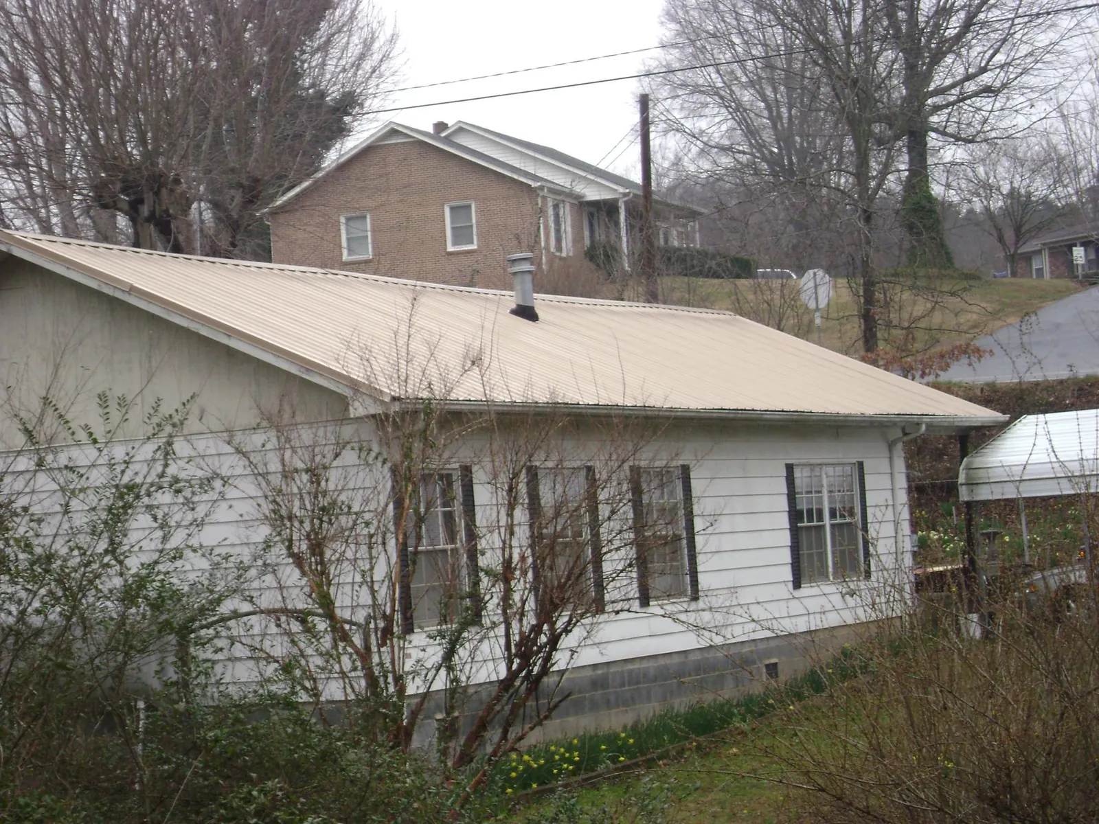 Tan metal roof on a white sided house set into a hillside — Commercial Roofing by Roofing Brothers in Hartington