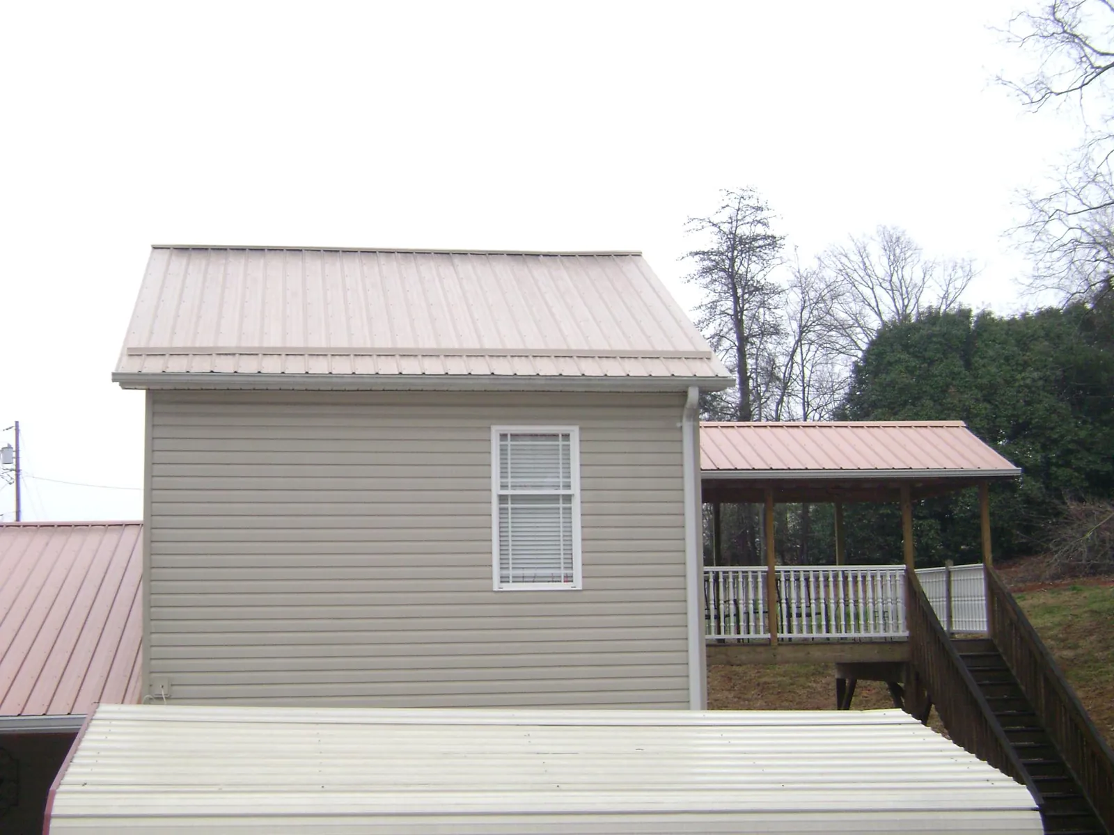 Tan metal roofs on a two story addition and attached porch, from a Roof Replacement job in Hartington
